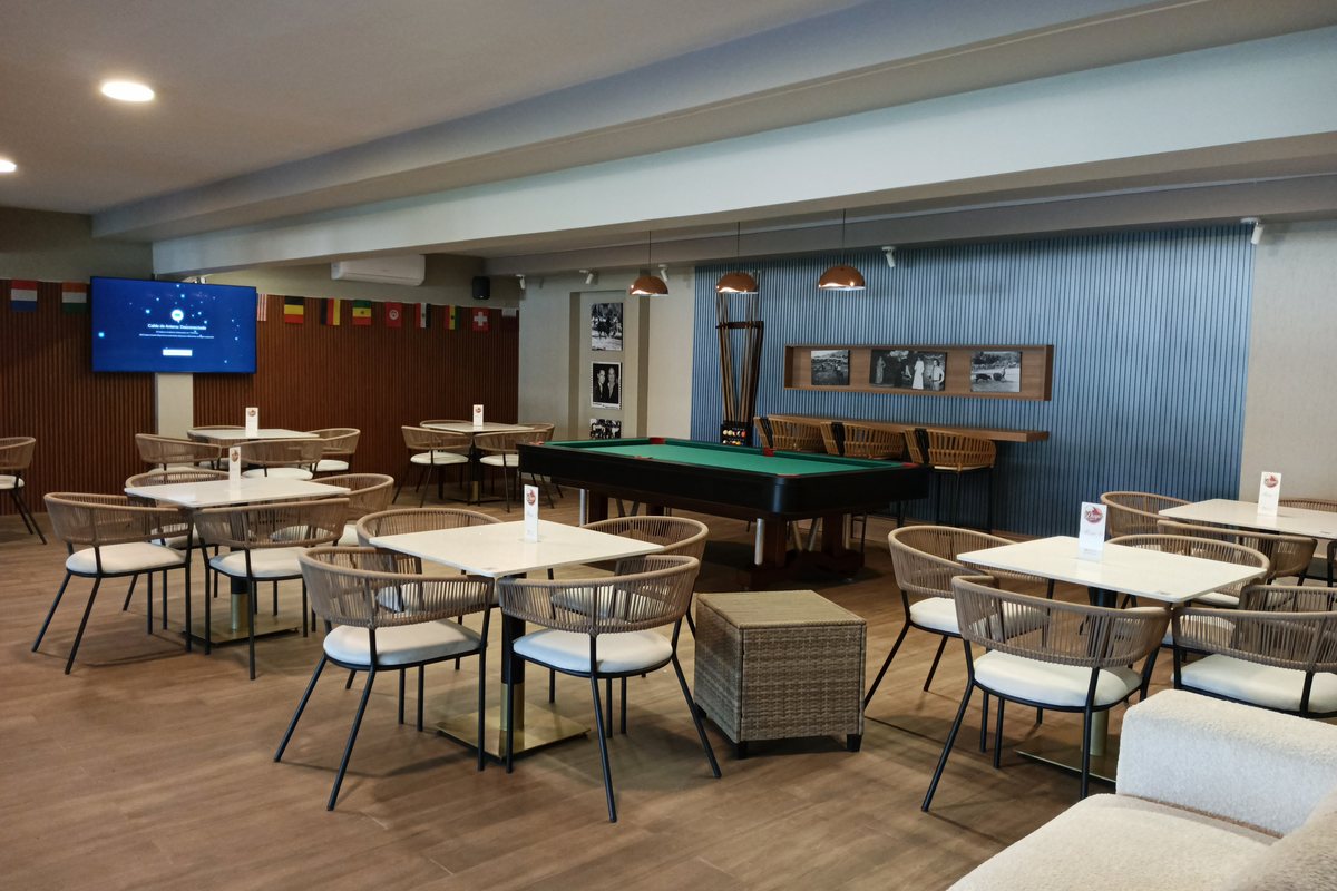 Salón del club con mesas redondas y una mesa de billar al fondo