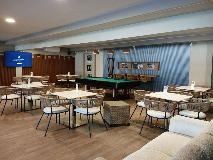 Salón del club con mesas redondas y una mesa de billar al fondo